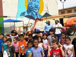 Gathering of people beneath mural of Rev. Martin Luther King
