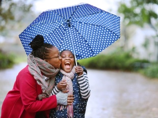 Black mother and daughter looking very happy while playing in the rain together. 